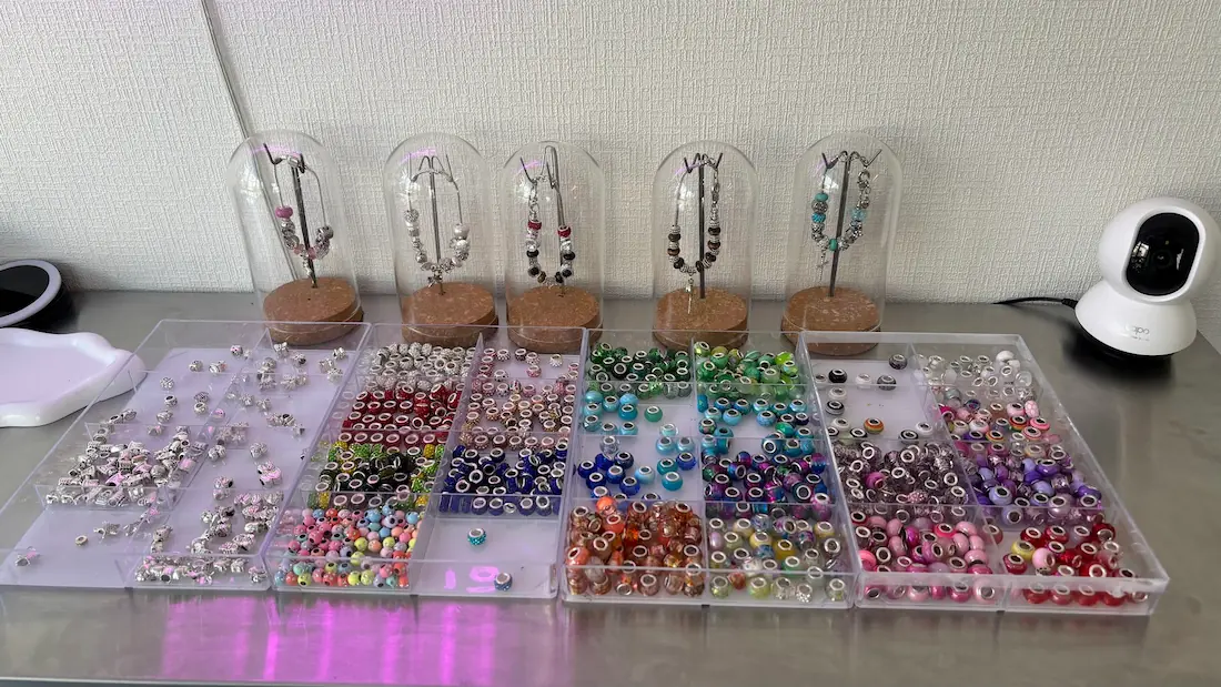 「BRACELET LAB.」の店内で、色鮮やかなカラフルビーズやシルバーパーツが収められたクリアケースと、ガラスドームに入ったブレスレットの完成見本が並んでいる様子。