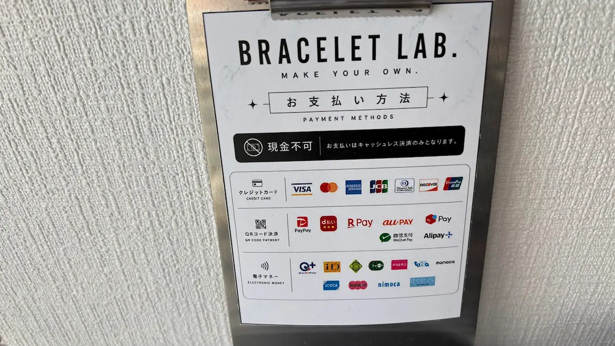 「BRACELET LAB.」のお支払い方法が記載された案内のアップ。中央に「現金不可」のアイコンと、クレジットカード、QRコード決済、電子マネーの対応ブランドのロゴが並んでいる様子。