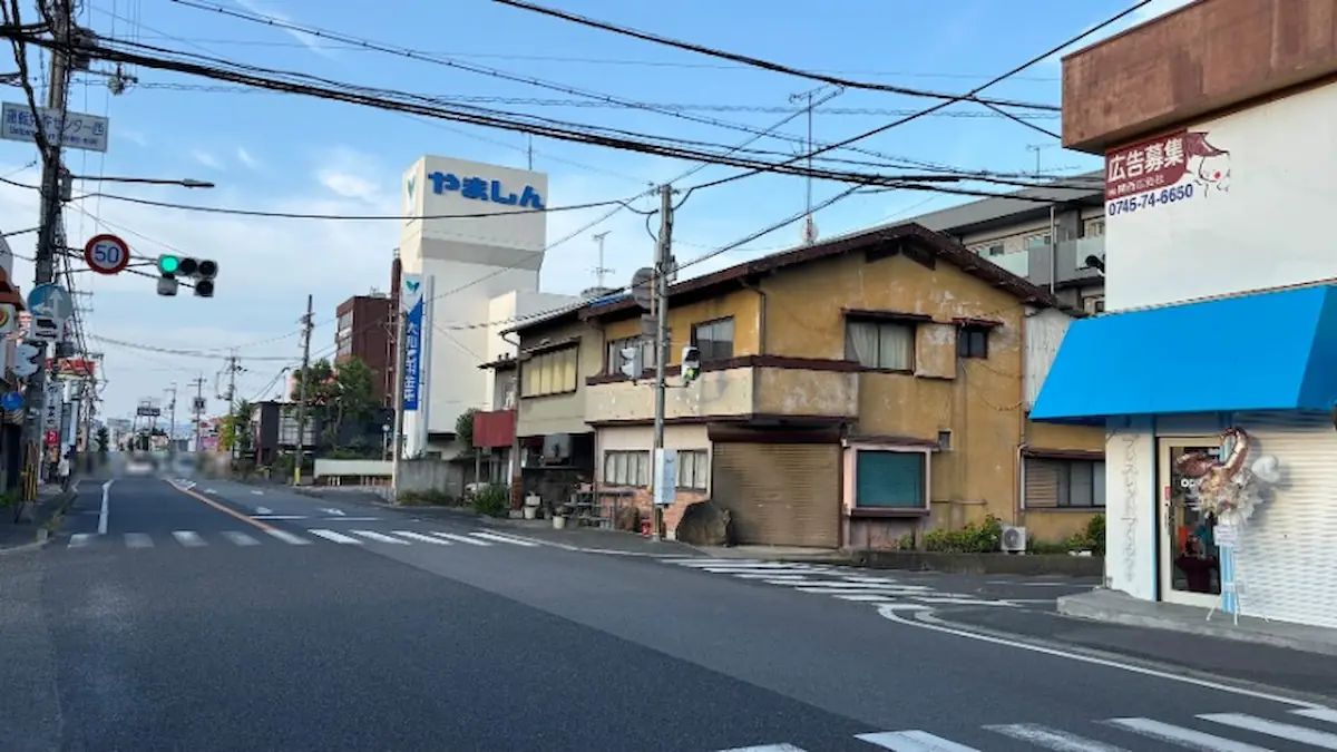 「BRACELET LAB.」の店舗前交差点から八木方面へ向かう道路の様子。遠方に「やましん」の大きな看板やビルが写っている。