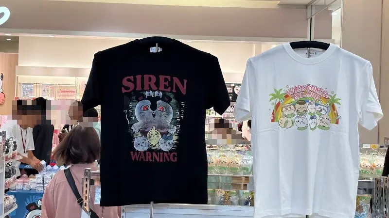 ちいかわPOP UP STOREで販売されている限定Tシャツ。「SIREN WARNING」と書かれたブラックのTシャツと、「WELCOME TO ISLAND」と書かれたホワイトのTシャツが展示されている様子
