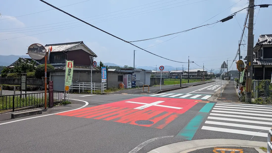 路面に赤く大きく塗装された十字の目印と横断歩道がある、藤原宮跡の臨時駐車場へ向かう最後の曲がり角となる交差点の様子。