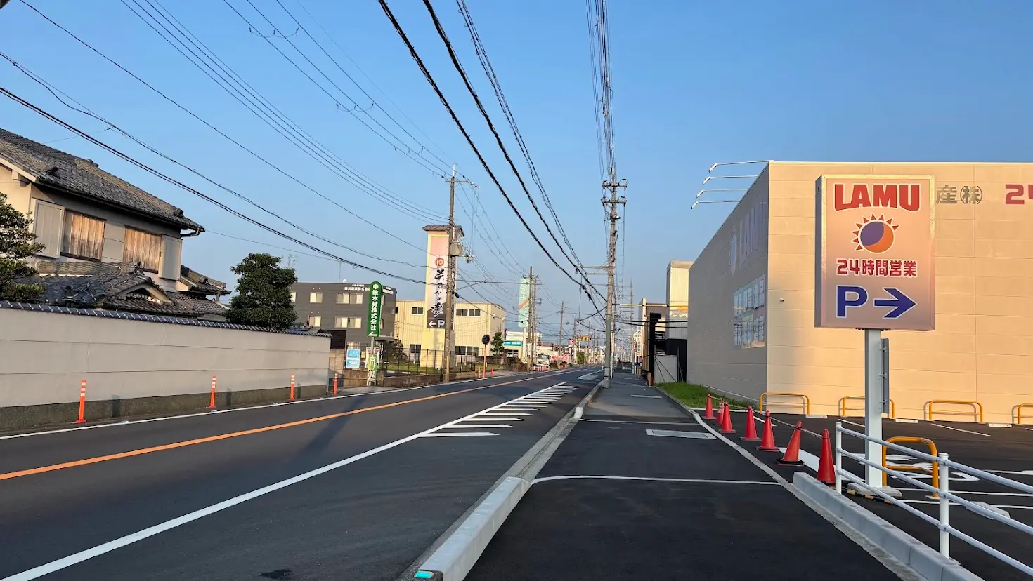 ラ・ムー橿原醍醐店の敷地そばから橿原市街方面を見た道路の風景。右手にラ・ムーの看板、前方には「あすかの湯」の看板や電柱が並ぶ