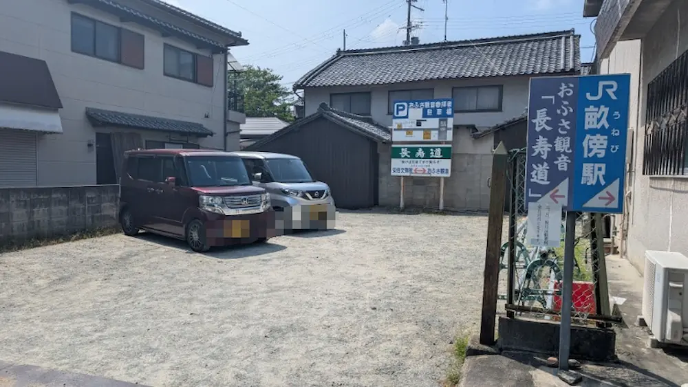おふさ観音の南駐車場の様子。駐車スペースに車が停まっており、周辺には「JR畝傍駅」「おふさ観音 長寿道」といった青い案内看板が掲げられている