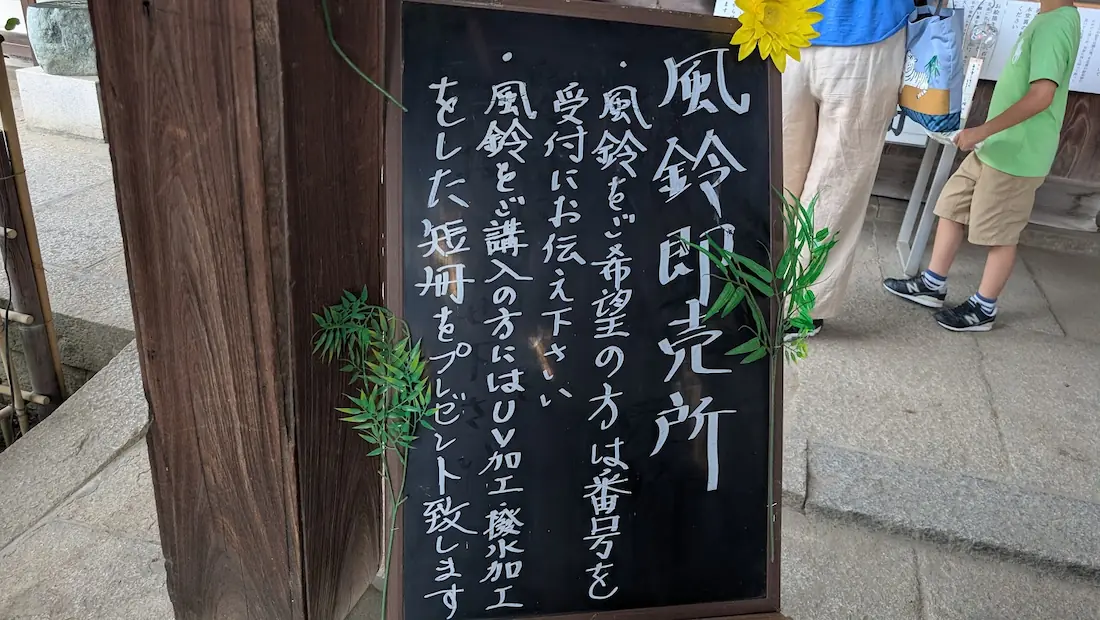 おふさ観音の境内にある「風鈴即売所」の案内黒板ボード。風鈴の購入方法やUV加工・撥水加工された短冊のプレゼントについて記載されている