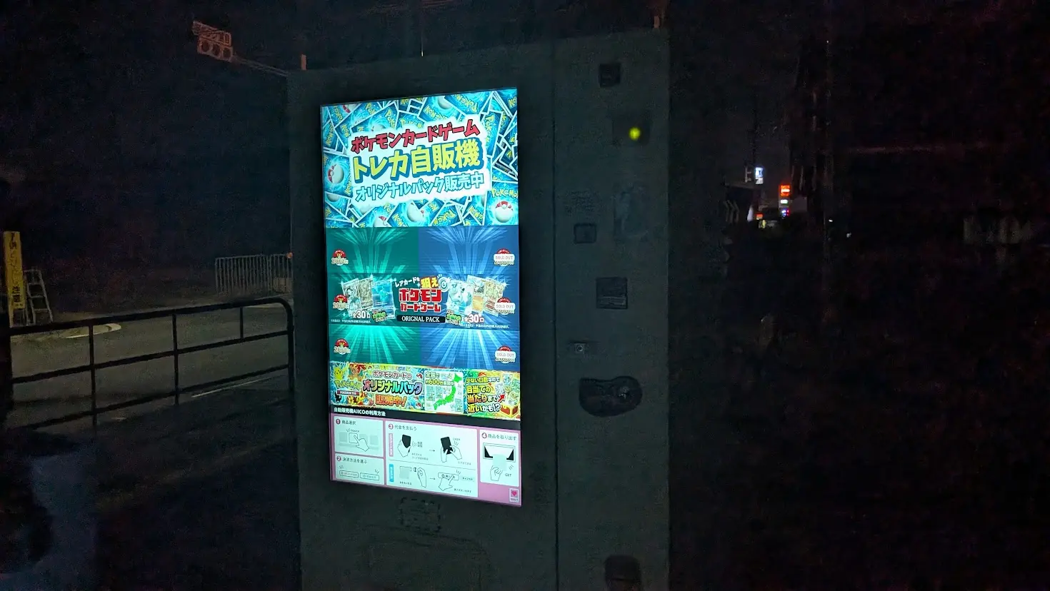 夜間に光り輝く「ポケモンカードゲーム トレカ自販機」。液晶画面には「オリジナルパック販売中」の文字や操作方法が表示されている