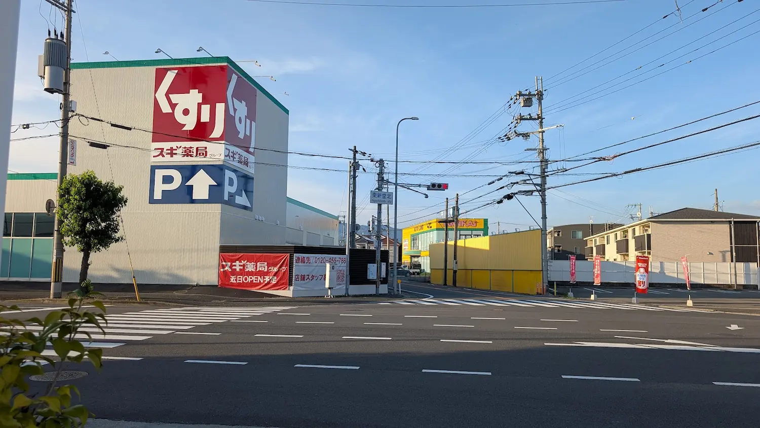 「東新堂北」交差点の風景。オープンを控えたスギ薬局の店舗建物と、大きく掲げられた「近日OPEN予定」の横断幕が写っている