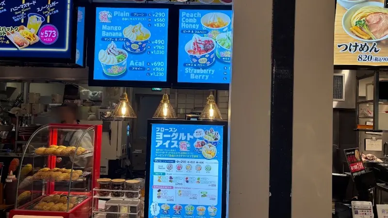 太陽のトマト麺橿原アルル店のショーケースに陳列されたチーズハットグ。奥にはフローズンヨーグルトアイスのメニュー掲示も見える