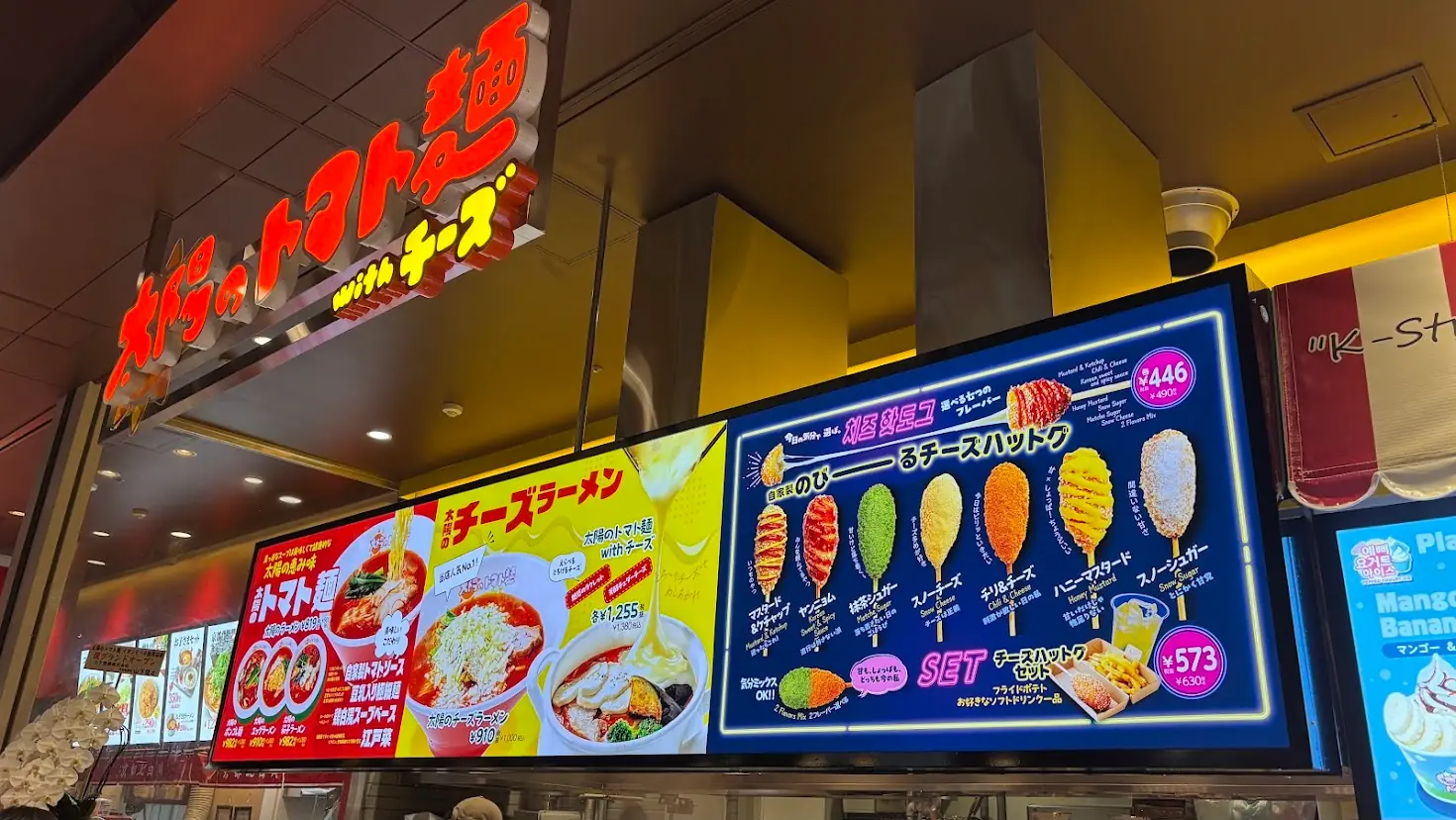 太陽のトマト麺 with チーズ 橿原アルル店の店頭看板。看板メニューのチーズラーメンと、自家製のびーるチーズハットグのラインナップが大きく掲示されている