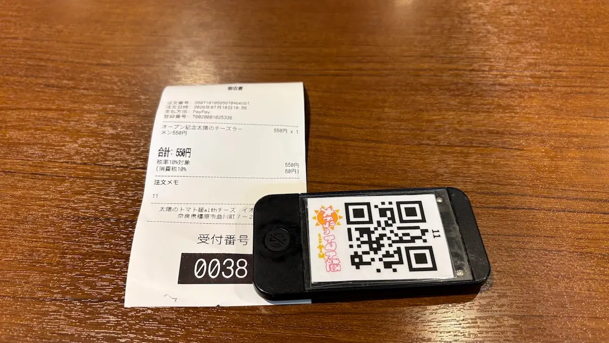 太陽のトマト麺橿原アルル店のレシートと受付番号札。支払い方法としてPayPayが記載されており、オープン記念のチーズラーメンの価格が確認できる