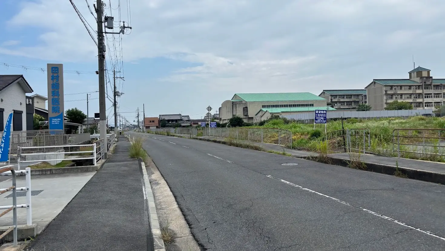 馬見丘陵公園方面を望む道路。左手には歯科医院の看板があり、右手には学校のような大きな建物が見える、閑静な風景