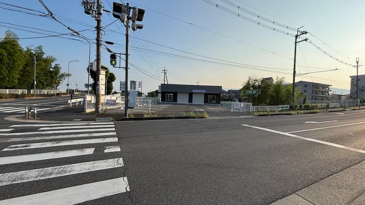 交差点から見たヨーグルトワールドの全景。中央に店舗の入口とロゴ、その手前にはしっかりと舗装された広々とした駐車場が広がっている