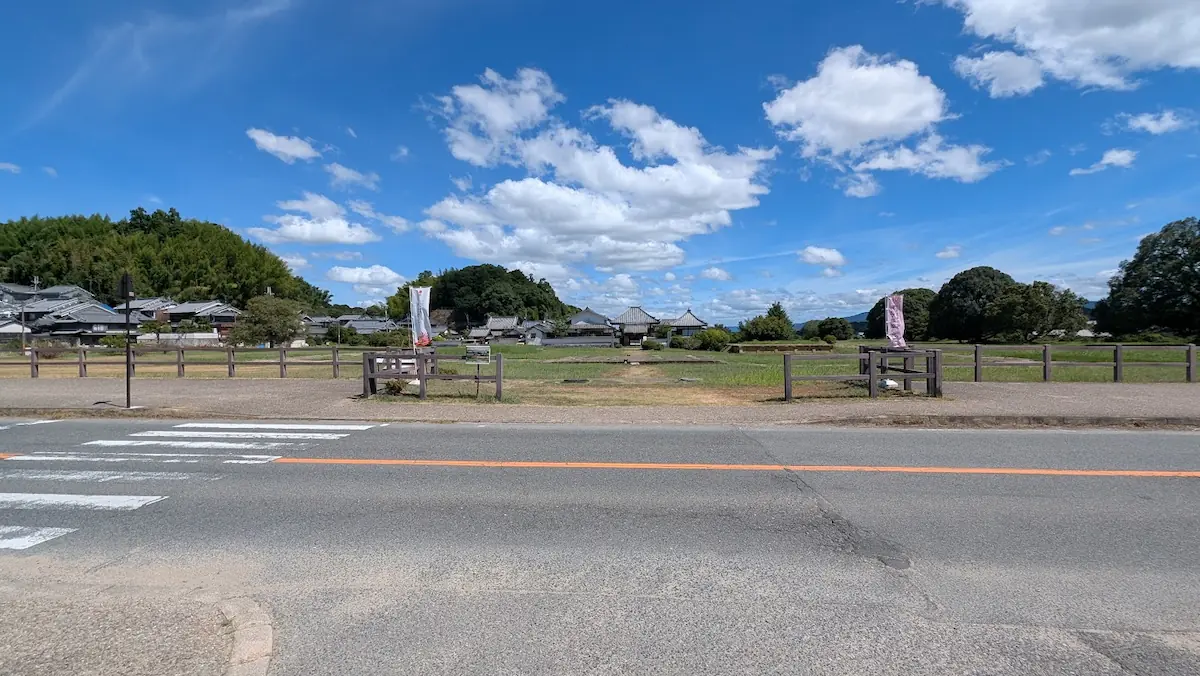 青空の下、奈良県明日香村の歴史的な寺院「川原寺跡」の境内全景と、手前の道路・横断歩道の様子。