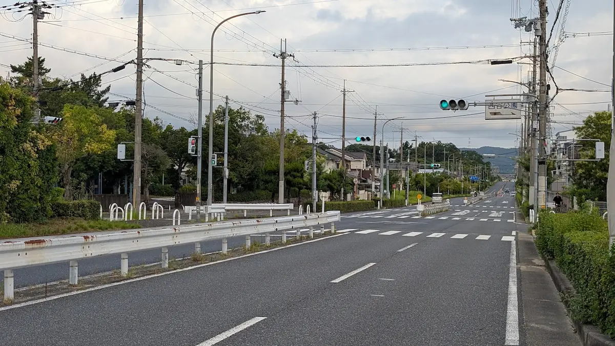 夕暮れの空の下、中和幹線の工事現場から香芝・真美ケ丘方面へ向かう車道と信号機の様子。道路脇にはガードレールや街路樹が整備されている。