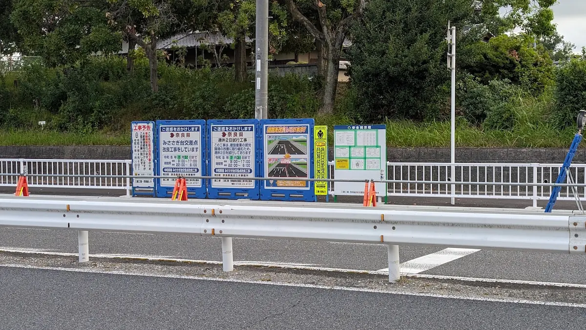 中和幹線のみささぎ台交差点付近に設置された、「道路を改良しています！」と施工前後の図や右折レーン新設の工事内容を伝える複数の青い案内看板と黄色い注意看板。