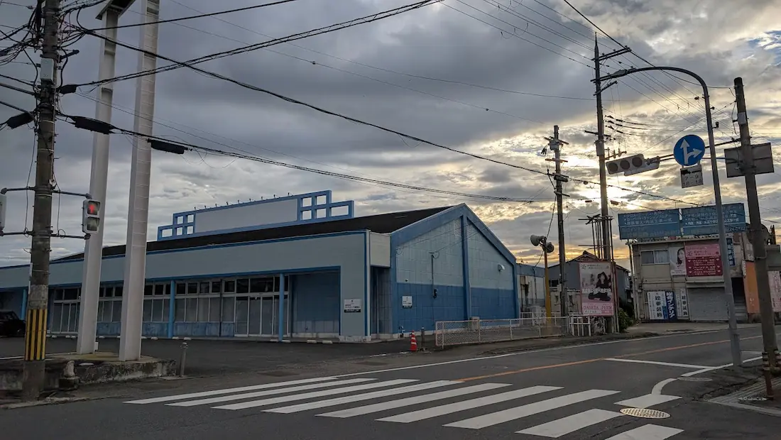 曇天の下、かつて釣り具店「マリーンコンパニオン」があった青い外観の建物と、国道165号線の出合交差点付近の様子。