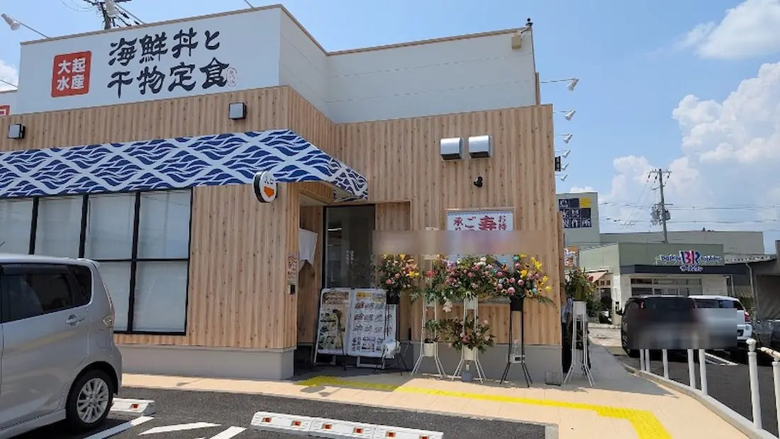 フレスポ桜井の新店「大起水産 海鮮丼と干物定食」の店舗入り口付近。開店祝いの華やかなスタンド花やメニュー看板が並び、真新しい木目調の外壁が広がる様子。