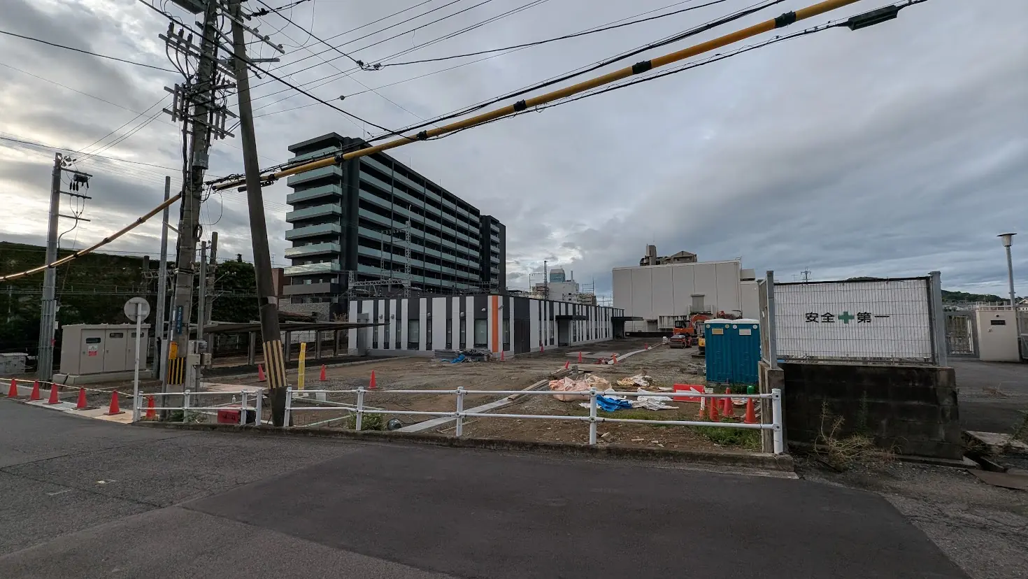 曇天の下、南八木一丁目の橿原変電所横で進められている工事現場の様子。フェンスやコーン、周囲の建物が写る遠景。