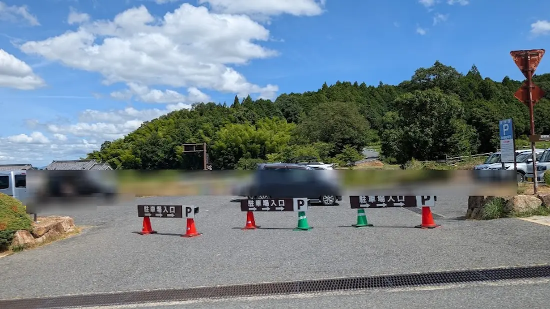 青空の下、緑豊かな山並みを背景に、数台の車が駐車され「駐車場入口」の看板とカラーコーンが並ぶ土曜日の石舞台古墳周辺の駐車場。