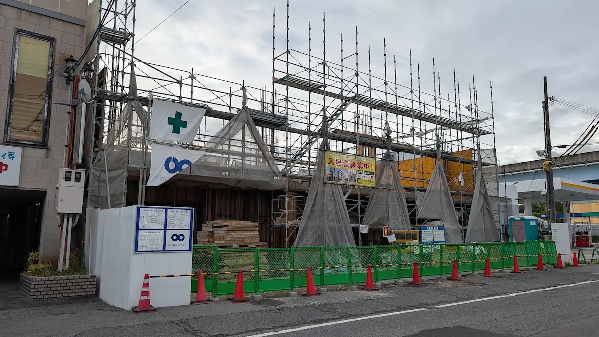 橿原市四条町で足場が組まれ、建築中の様子がうかがえるマンションの建設現場の正面からの様子。緑のフェンスやカラーコーンが設置されている。