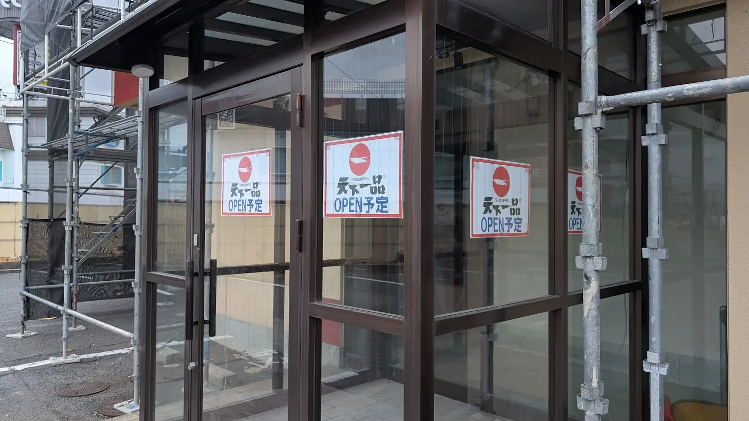 ガラス張りの店舗入口ドアに、「天下一品 OPEN予定」と書かれた複数の赤いロゴ入り張り紙が貼られている様子。