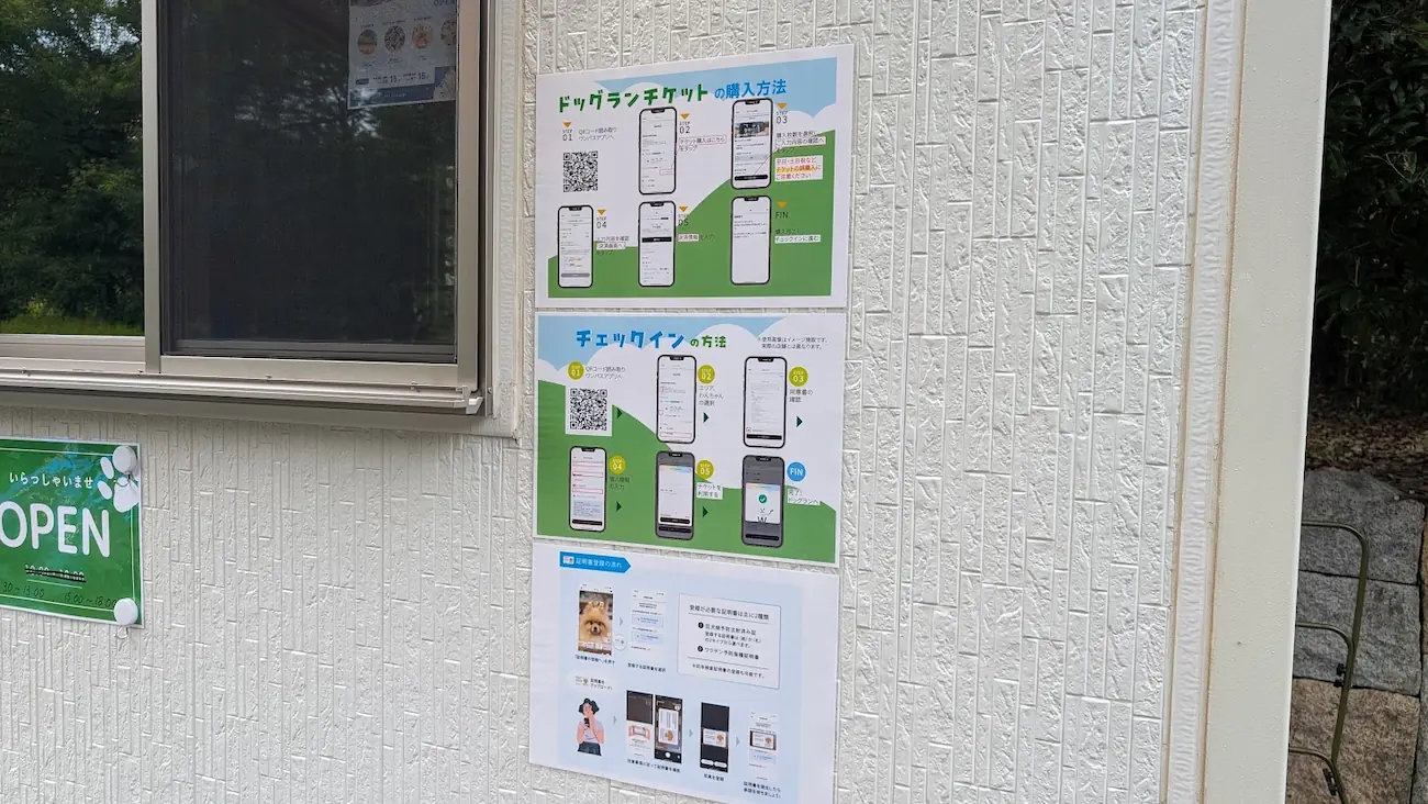 馬見丘陵公園の新設ドッグラン「UMAMI WAN Park」の受付壁面に掲示された、スマホアプリによるチケット購入方法、チェックイン手順、証明書登録の流れを解説するポスターの様子。