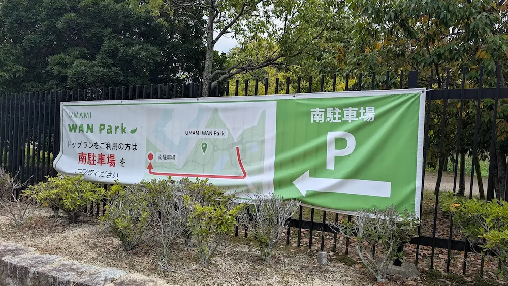 馬見丘陵公園内に新設されたドッグラン「UMAMI WAN Park」の案内幕。南駐車場への案内図と「南駐車場 P」の文字、左向きの矢印が緑色のバナーに記載されている様子。
