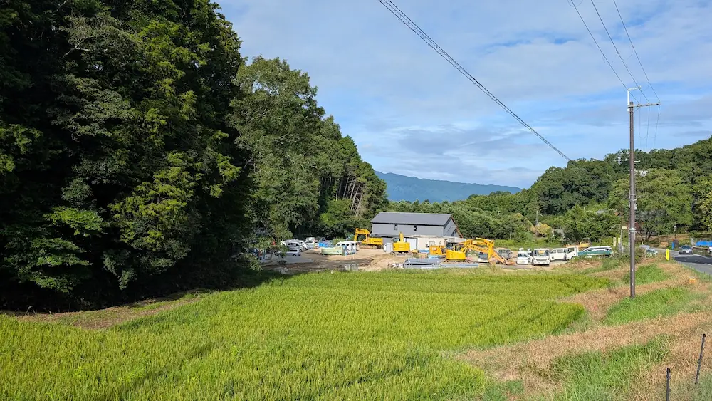 飛鳥村の徒歩ルートの途中、豊かな緑と田園風景の中に広がる「星のや飛鳥」の建設現場と重機の様子。