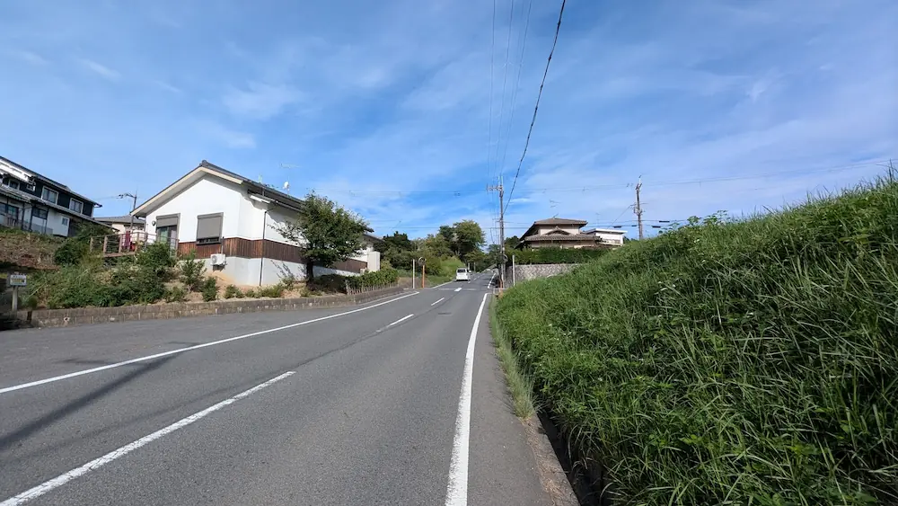 青空の下、星のや飛鳥への徒歩ルートの途中にある、住宅街を抜けながら奥へと緩やかに上り続ける坂道の様子。