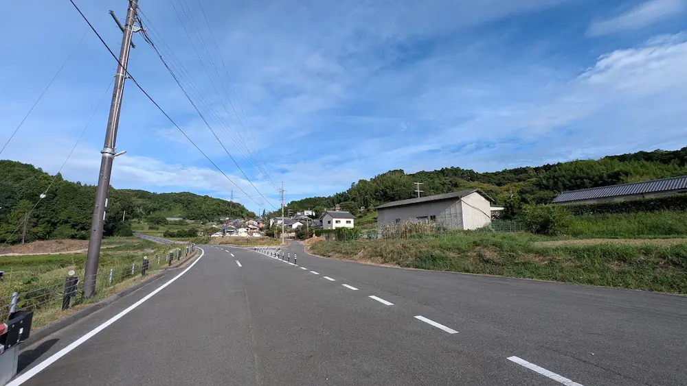 青空の下、マルコ山古墳の周辺で新しく建設・整備されたアスファルトの道路と周辺の田園風景の様子。