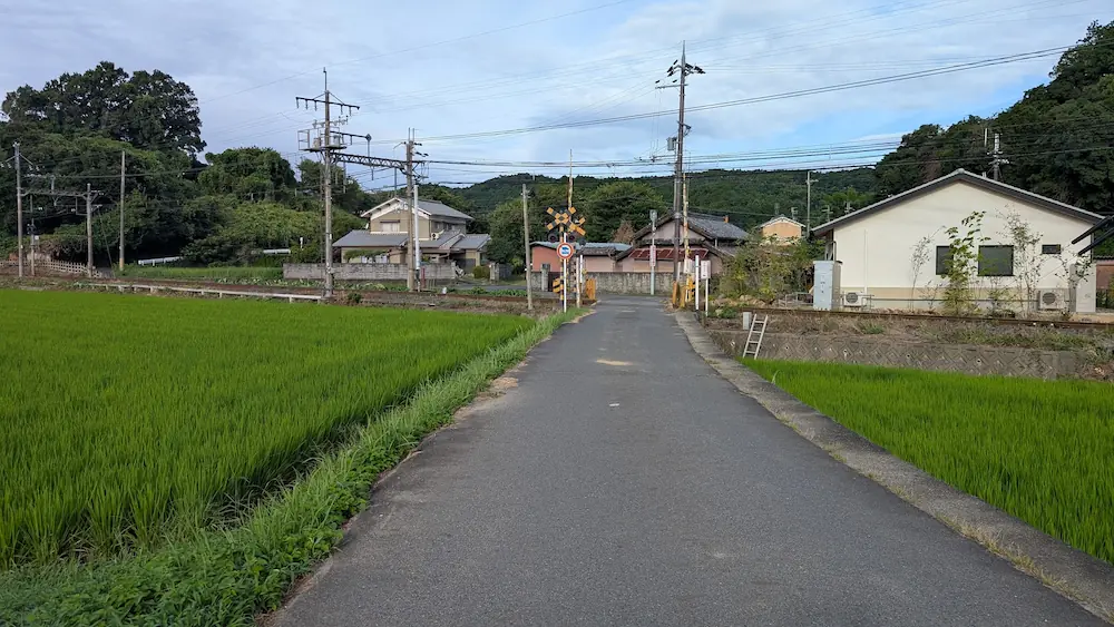 マルコ山古墳への徒歩ルートの途中、田園地帯と踏切が広がるのどかな舗装道路の様子。