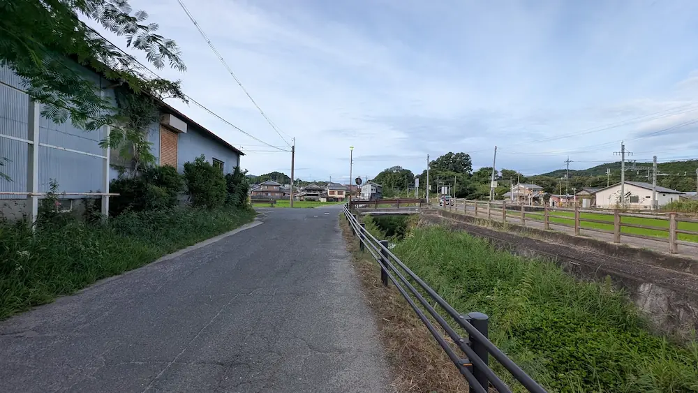 マルコ山古墳への徒歩ルートの途中、川沿いに続くのどかなアスファルトの道路と田園風景の様子。