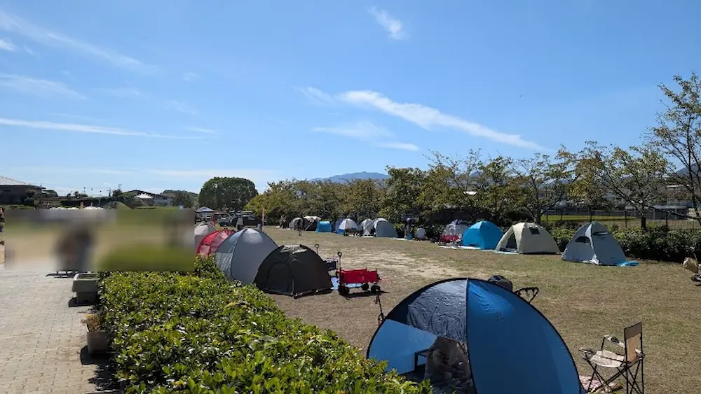 竹取公園のほほえみフェスタ会場脇の芝生広場に、多くのファミリーがテントを張りくつろいでいる様子。