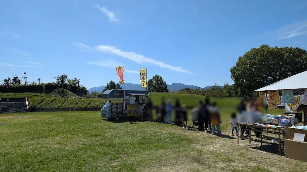 竹取公園のほほえみフェスタ会場の芝生広場に停車し、多くの来場者が長い行列を作っているキッチンカー「とらじろう」の全体像。